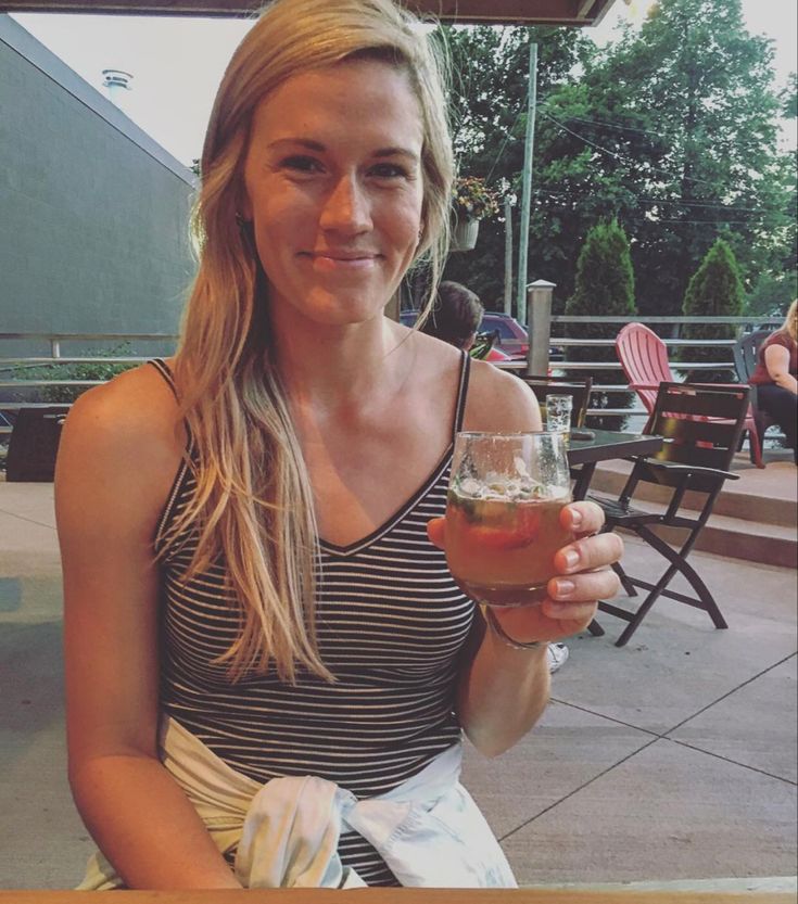 a woman sitting at a table with a drink in her hand - Annie Drews’s Height: Volleyball Star’s Towering Stature